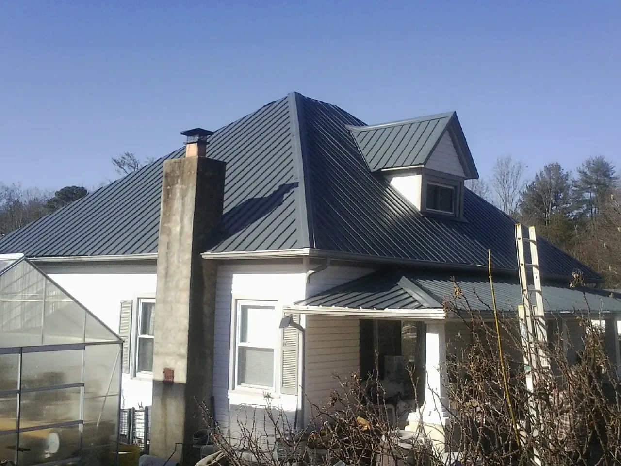 Dark blue standing seam metal roof on a white farmhouse with dormer — Slate & Tile Roof Repair by Roofing Brothers in Eunice