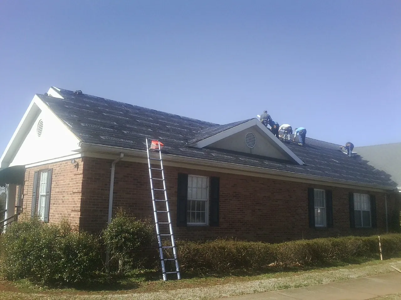 Crew tearing shingles off a brick ranch roof with a ladder set — Emergency Roof Repair work by our crew in Eunice