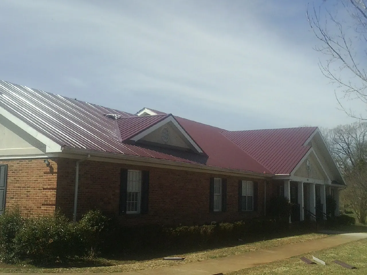 Red metal roof with gabled entries on a long brick building, from a Hail Damage Roof Repair job in Eunice