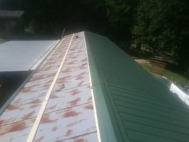 Old rusted panels beside newly installed green metal roofing — Wind Damage Roof Repair by Roofing Brothers in Eunice