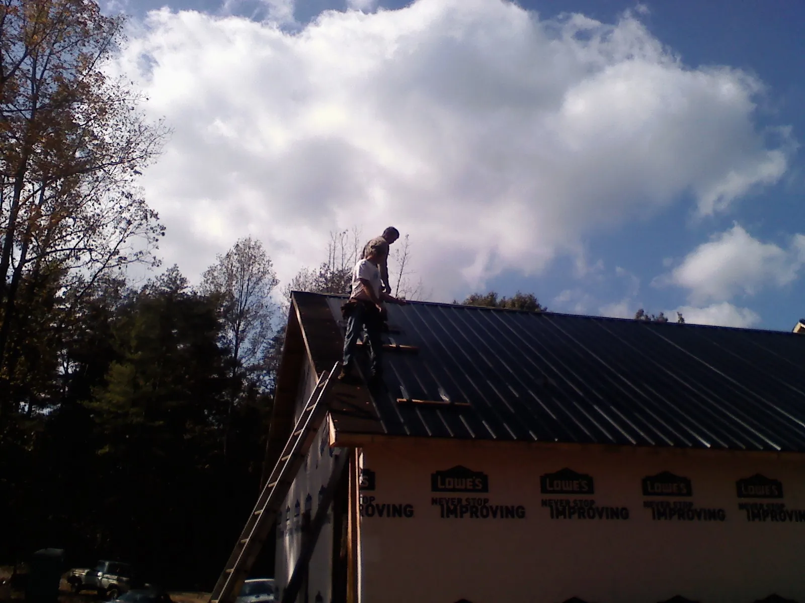 Roofer fastening dark metal panels high against a cloudy sky, from a Roof Inspection job in Eunice