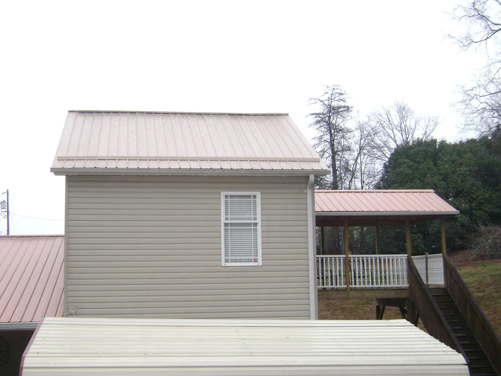Tan metal roofs on a two story addition and attached porch, from a Roof Replacement job in Eunice